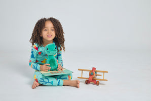 Child holding Tiny T. Rex plush doll while sitting with a book and toy airplane
