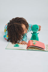 Child reading with a green Tiny T. Rex plush doll and an open picture book