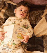 Baby wearing bunny print coverall holding "Guess How Much I Love You" book