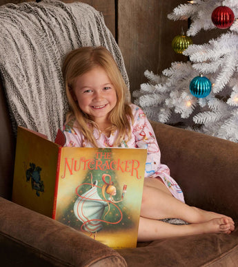 Smiling child in Nutcracker nightdress reading by a Christmas tree